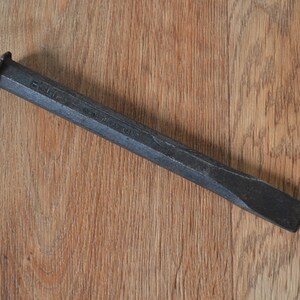 May include: A black metal chisel with a rounded head and a rectangular blade. The chisel is made in England.