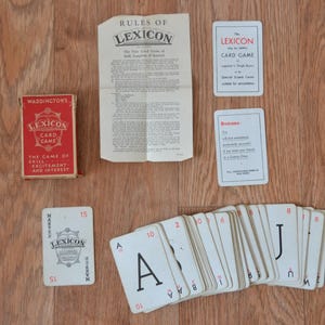Könnte beinhalten: Ein Waddingtons Lexicon Kartenspiel-Set bestehend aus einer roten Schachtel, einem gefalteten Anleitungsblatt, zwei kleinen weißen Informationskarten und einer Sammlung weißer Spielkarten mit schwarzen Buchstaben und Zahlen, darunter ein A, ein J und eine 15.