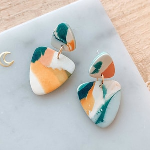 May include: A pair of abstract, colorful, triangle-shaped earrings with a marbled design in shades of green, blue, orange, and pink.