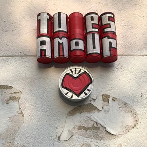 May include: A white wall with the word "TU ES AMOUR" spelled out in black and white letters on red painted tin cans. A red heart is painted on a tin can below the word.