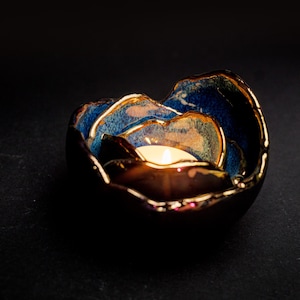 Può includere: Un portacandele in ceramica blu e oro a forma di fiore con una piccola candela bianca all'interno.