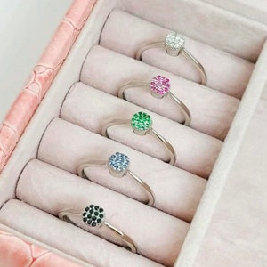 May include: Five silver rings with different colored gemstones in a pink ring box. The gemstones are black, blue, green, pink, and white.