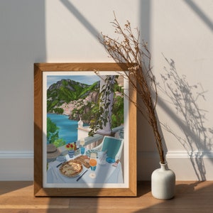 Puede incluir: Una impresi&oacute;n enmarcada de una vista panor&aacute;mica de una ciudad costera con un balc&oacute;n con vistas al mar. El balc&oacute;n tiene una mesa preparada para una comida con una pizza, bebidas y un plato de fruta.