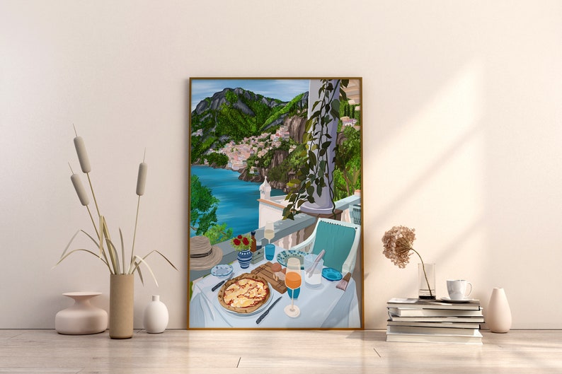 Puede incluir: Una ilustraci&oacute;n enmarcada de una mesa puesta con una pizza, un vaso de zumo de naranja y un sombrero en un balc&oacute;n con vistas a una ciudad costera con colinas verdes en el fondo.