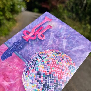 Puede incluir: Una tarjeta de cumplea&ntilde;os rosa y morada con una bola de discoteca y una vela rosa sobre un soporte azul. El fondo es una acuarela rosa y morada.