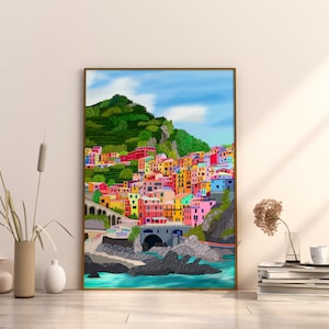 May include: A colourful painting of a seaside town with brightly coloured buildings on a hillside. The town is nestled between a green hill and the blue ocean. The painting is framed in a gold frame.