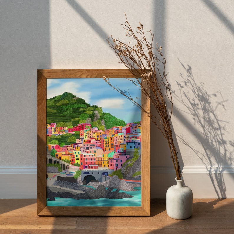 May include: A framed print of a colourful illustration of a seaside town with buildings on a hillside. The town is painted in shades of pink, yellow, blue, green, and red. The water is a deep blue and there are green hills in the background.