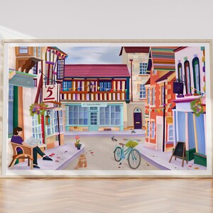 May include: A framed art print depicting a quaint European street scene. The artwork features colorful buildings, a bicycle, and a person reading a newspaper. The buildings have red, orange, and blue facades. The print is displayed on a wooden floor.
