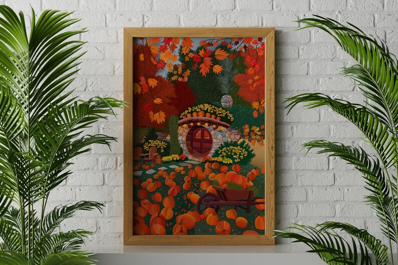 May include: A framed illustration of a stone cottage with a red door surrounded by autumn foliage and pumpkins. The cottage has a round window and a stone chimney. The pumpkins are scattered around the cottage and a wheelbarrow is in the foreground.
