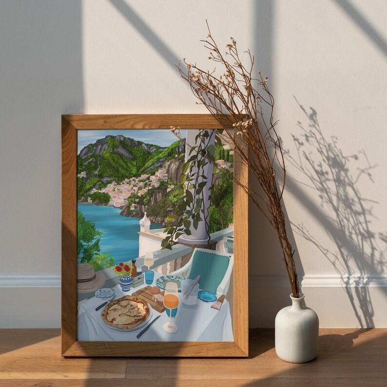 Puede incluir: Una pintura enmarcada que representa una mesa puesta con una pizza, un vaso de zumo de naranja y una vista de una ciudad costera en el fondo. La pintura est&aacute; colocada contra una pared blanca con un arreglo de flores secas en un jarr&oacute;n blanco.