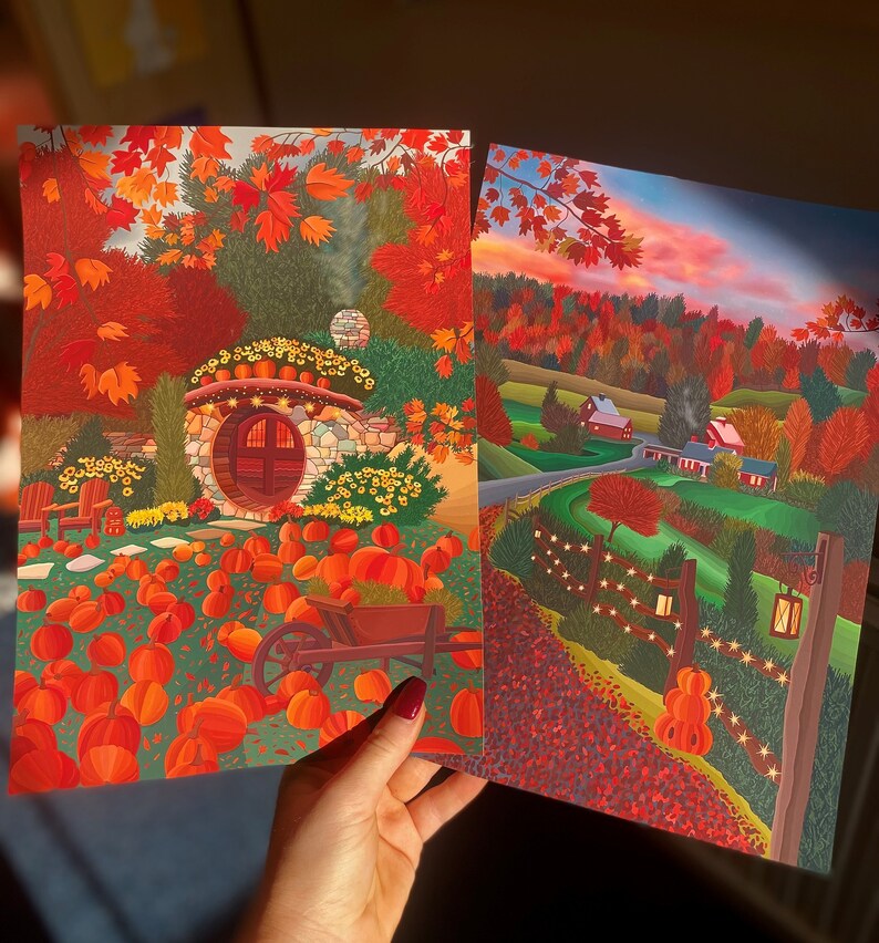 May include: Two paintings depicting autumn scenes. The first painting shows a small stone house with a round door surrounded by pumpkins and autumn foliage. The second painting shows a rural landscape with a farmhouse and a fence with fairy lights.