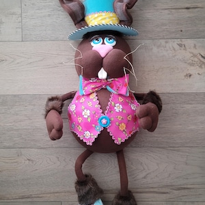 May include: A brown bunny wearing a blue and yellow hat, a pink vest with floral print, and blue roller skates. The bunny has a pink nose and blue eyes.