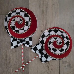 May include: Two red and white checkerboard lollipop decorations with gold trim and black and white bow ties. The lollipops are on red and white striped sticks.