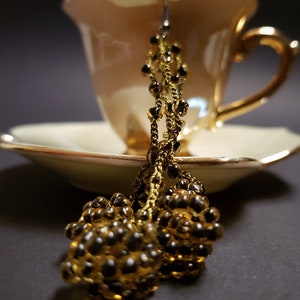 Könnte beinhalten: Ein Paar goldene Perlenohrringe mit Quasten-Design. Die Ohrringe hängen an einer Teetasse.