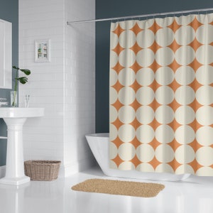 May include: A shower curtain with a repeating pattern of large, cream-colored circles set within a rust-orange diamond shape. The curtain hangs in front of a white bathtub. A beige bath mat is on the floor.