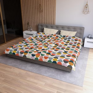 May include: A bed with a colorful, geometric patterned comforter. The design features semi-circles in shades of orange, yellow, green, blue, and gray on a white background. The bed is made up with two pillows and a gray bed frame.