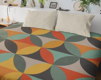 May include: A bed with a colorful geometric patterned duvet cover. The design features overlapping circles in shades of orange, yellow, teal, gray, and beige. Two cream-colored pillows rest on top. The room has a minimalist aesthetic.
