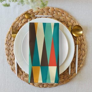 May include: A white dinner plate with a white rim and a geometric pattern napkin in shades of teal, brown, orange, and yellow. The plate is on a woven placemat.
