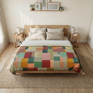 May include: A bed featuring a quilt with a multi-colored patchwork pattern of rectangular blocks. Each block contains fine vertical stripes in shades of red, green, yellow, orange, and blue. The bed has two light gray pillows and a white top sheet.