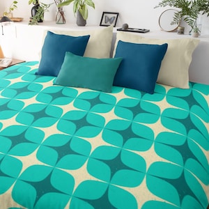 以下が含まれることがあります： ターコイズとクリーム色の掛け布団カバーで、重なり合った円形の幾何学模様が施されています。掛け布団カバーは、ターコイズとクリーム色の枕のあるベッドの上に置かれています。