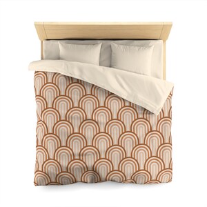 May include: A bed with a light wood headboard, two white pillows, and a cream-colored duvet. The duvet cover features a repeating pattern of arched shapes in shades of brown, tan, and cream, creating a retro design.