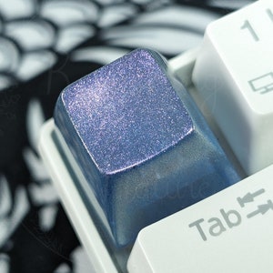Könnte beinhalten: Eine blaue und silberne, glitzernde Tastaturkappe mit einer weißen Tastatur im Hintergrund. Die Tastaturkappe ist mit "Tab" und Pfeilen nach links und rechts beschriftet.
