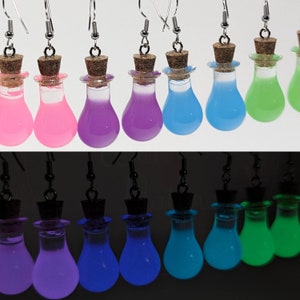 May include: A set of eight glow-in-the-dark earrings featuring small glass bottles filled with colorful liquid. The bottles have cork stoppers and silver hooks. The earrings are shown in both regular and dark lighting.