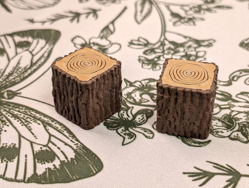 May include: Two brown wooden log slices with a light brown wood grain pattern on the top. The log slices are on a white background with a floral pattern.