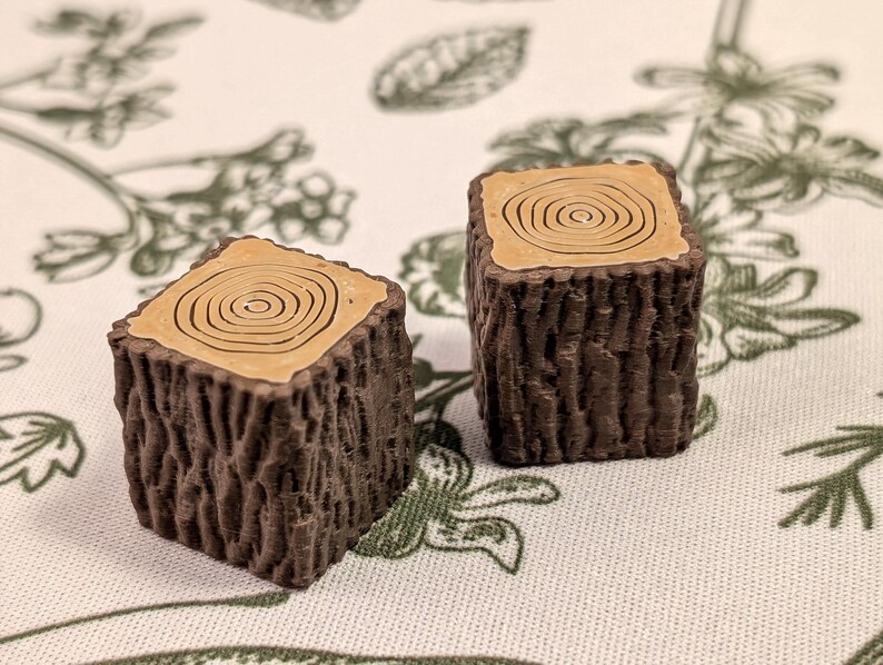 May include: Two brown wooden tree stump shaped blocks with a light brown wood grain pattern on the top.