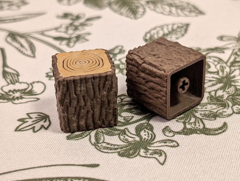 May include: Two brown wooden keycaps with a tree bark texture. One keycap has a light brown wood grain pattern on the top.
