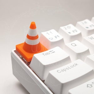 Pode incluir: Um teclado branco com uma tecla de cone de trânsito laranja. O cone está na tecla "Tab".