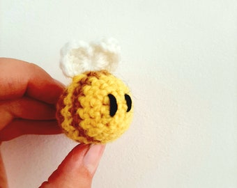 May include: A crocheted bee toy with yellow and brown stripes, white wings, and black eyes.