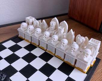 May include: A unique chess set with white pieces featuring skull and gothic architectural designs. The chess pieces are arranged on a black and white checkered board. The pieces have gold accents.