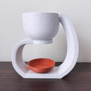 May include: White ceramic diffuser with a curved design. The top bowl is removable and the bottom bowl is a terracotta color.