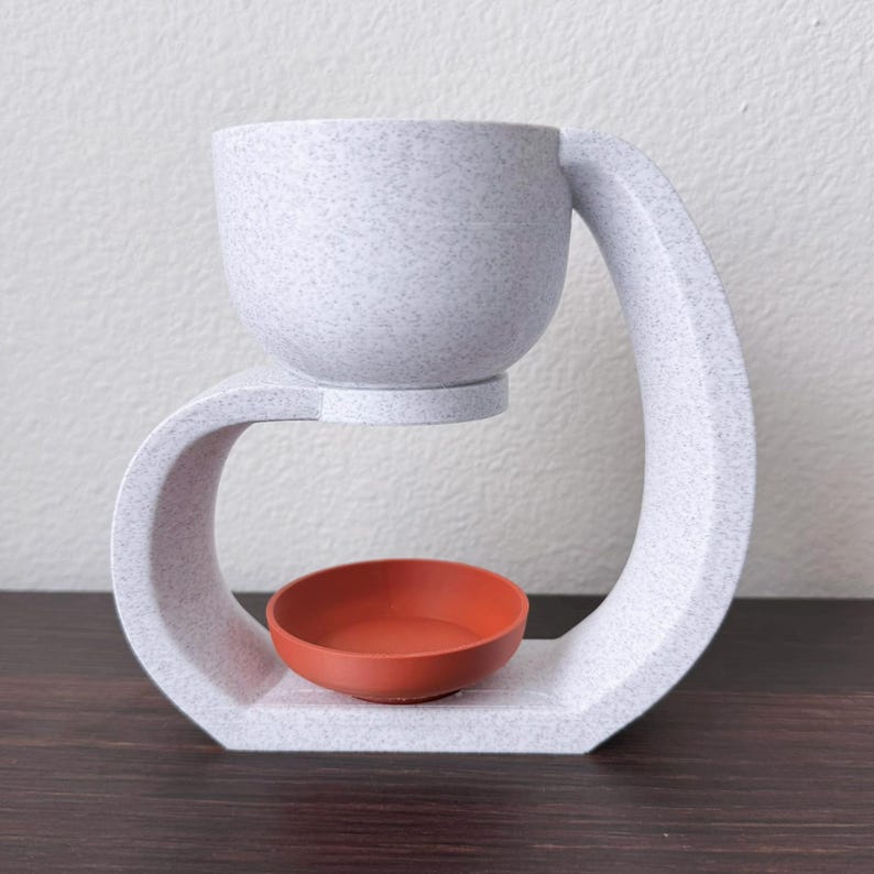 May include: White ceramic diffuser with a curved design. The top bowl is removable and the bottom bowl is a terracotta color.