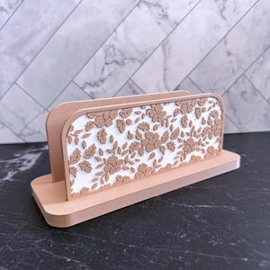 May include: A decorative desk organizer in a light brown color. The organizer features a floral design on a white background. The design is made of flowers and leaves. The organizer is made of a sturdy material and is designed to hold papers or other desk items.
