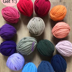 May include: A collection of colorful t-shirt yarn balls in various shades, including red, pink, orange, purple, green, and blue. The text "Buy 3 Get 1 :)" is in a pink circle in the upper left corner. The yarn balls are arranged on a wooden surface.