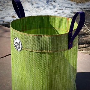 May include: A green woven fabric planter with purple handles. The planter has a small white label with a cartoon image of a bearded man.