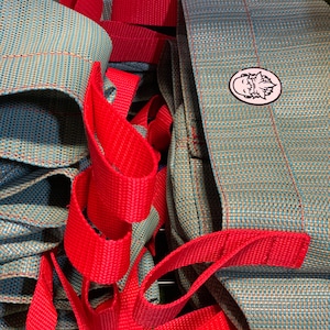 May include: A close-up of a set of blue and red woven fabric bags. The bags have a red strap and a small logo with a cartoon face on them.