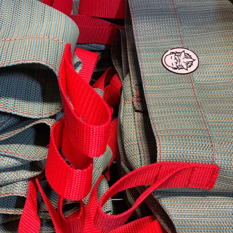 May include: A close-up of a set of blue and red woven fabric bags. The bags have a red strap and a small logo with a cartoon face on them.