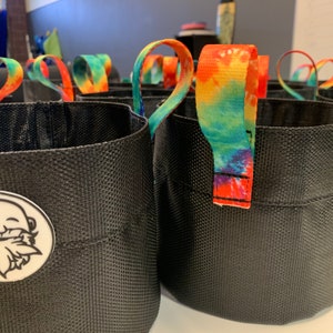 May include: A set of black fabric plant pots with tie-dye handles. The pots have a textured surface and a logo of a cartoon beard on one of the pots.