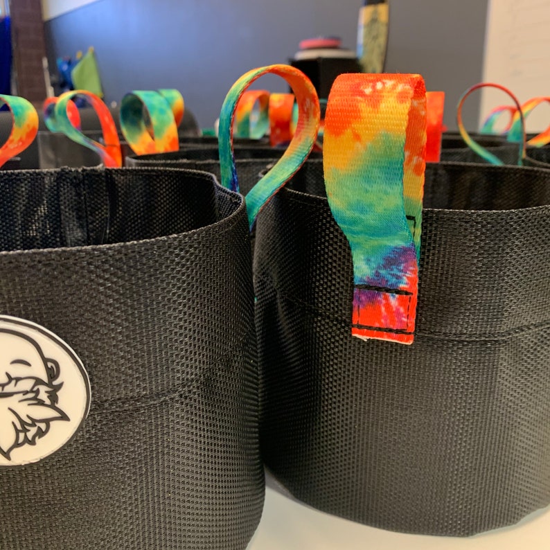 May include: A set of black fabric plant pots with tie-dye handles. The pots have a textured surface and a logo of a cartoon beard on one of the pots.