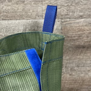 May include: A green reusable shopping bag with a blue handle. The bag is made of a woven material and has a blue lining.