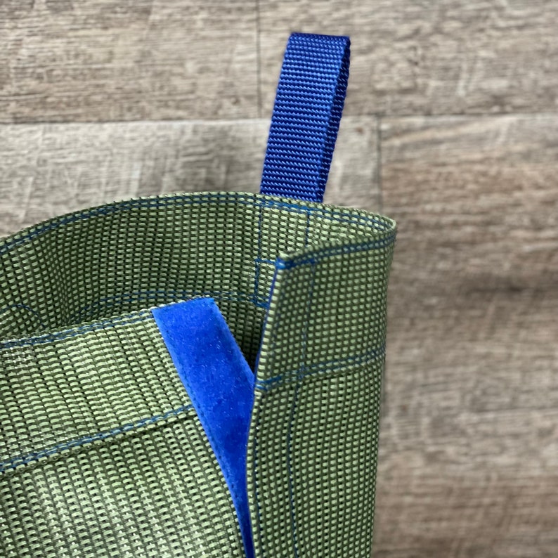 May include: A green reusable shopping bag with a blue handle. The bag is made of a woven material and has a blue lining.