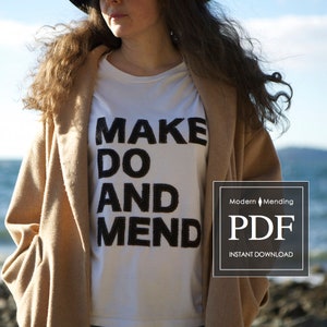 Puede incluir: Una camiseta blanca con las palabras "MAKE DO AND MEND" en letras negras cosidas. La camiseta la lleva puesta una persona con el pelo largo y castaño y un abrigo marrón. La imagen también incluye una etiqueta de descarga digital con el texto "Modern Mending PDF INSTANT DOWNLOAD".
