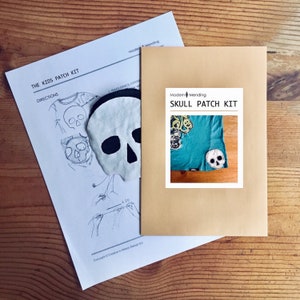 May include: A brown envelope with the text "Modern Mending Skull Patch Kit" printed on the front. The envelope contains a white felt skull patch and instructions for making a patch.