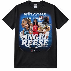 Puede incluir: Camiseta negra con un diseño gráfico que presenta el texto "WELCOME TO THE A" y "ANGEL REESE". El diseño incluye imágenes de jugadoras de baloncesto y el logotipo de la WNBA. La camiseta está hecha de un material suave.