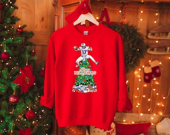 May include: Red Christmas sweatshirt with a green Christmas tree and a football player on top. The tree is decorated with football-themed ornaments and the text "Merry Billsmas".