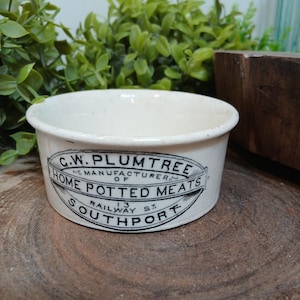 May include: A cream-colored ceramic pot with black printed text that reads C.W. PLUMTREE MANUFACTURER OF HOME POTTED MEATS 13 RAILWAY ST. SOUTHPORT. The container has a round shape with a smooth finish and a slightly speckled surface texture.