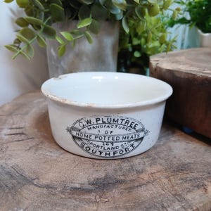 May include: A white ceramic pot with a black printed label that reads C.W. PLUMTREE MANUFACTURER OF HOME POTTED MEATS 164 PORTLAND ST SOUTHPORT. The round container features a smooth finish with minor brown discoloration along the top rim edge.